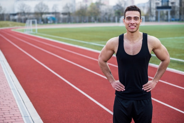 Portrait d'un jeune athlète masculin souriant, debout sur la piste de course