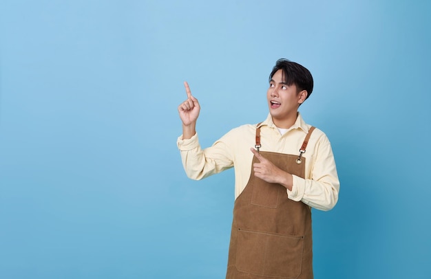 Portrait d'un jeune barista asiatique portant un tablier debout et montrant du doigt une publicité