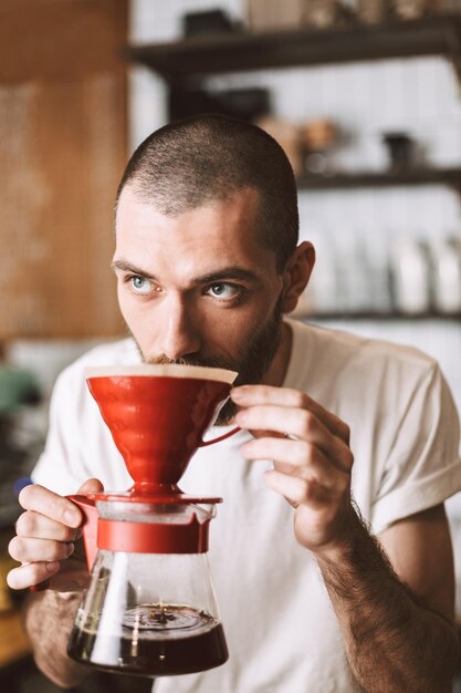 Portrait de jeune barista debout au comptoir du bar et sentant verser du café tout en regardant pensivement de côté dans le café