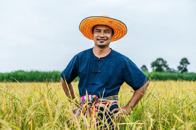 Portrait jeune beau fermier dans une rizière, il porte un chapeau de paille, il sourit et se tient sur la taille