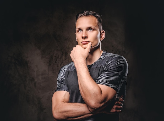 Portrait d'un jeune beau sportif tient la main sur le menton sur un fond sombre.