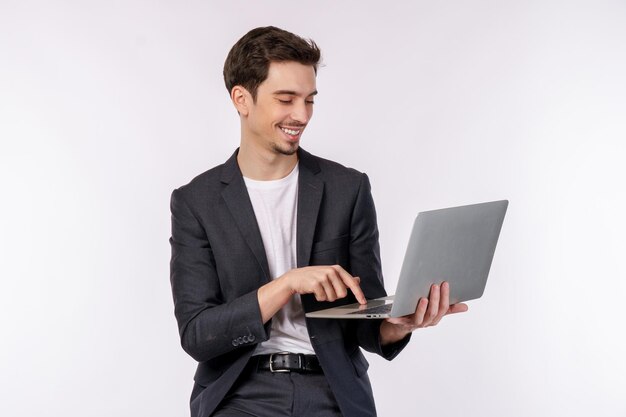 Portrait de jeune bel homme d'affaires souriant tenant un ordinateur portable dans les mains en tapant et en parcourant des pages Web isolées sur fond blanc