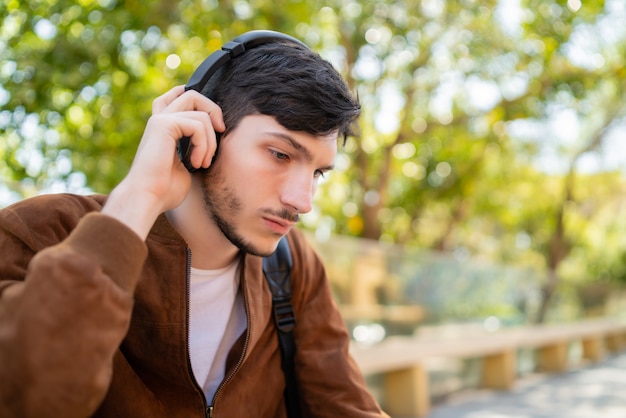 Portrait de jeune bel homme écoutant de la musique avec des écouteurs alors qu'il était assis à l'extérieur. Concept urbain.