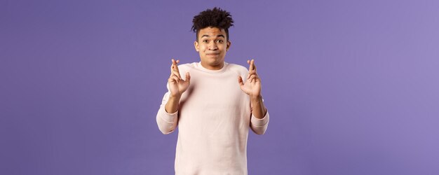 Portrait d'un jeune bel homme plein d'espoir avec des dreads annonçant que quelque chose de bien se passe, croise les doigts