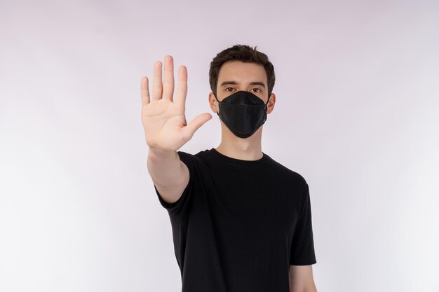 Portrait de jeune bel homme portant un masque médical faisant arrêter de chanter avec la paume de la main sur fond blanc