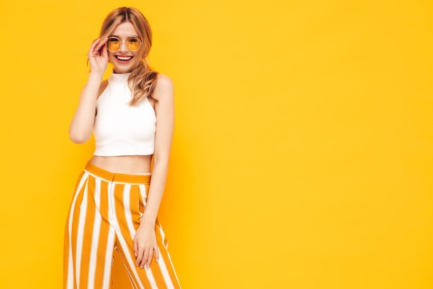 Portrait de jeune belle femme blonde souriante dans des vêtements d'été à la mode femme insouciante posant près d'un mur jaune en studio Modèle positif s'amusant à l'intérieur Enthousiaste et heureux