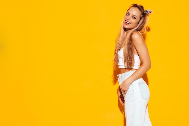 Portrait de jeune belle femme blonde souriante dans des vêtements d'été à la mode Sexy femme insouciante posant près d'un mur jaune en studio Modèle positif s'amusant à l'intérieur Enthousiaste et heureux