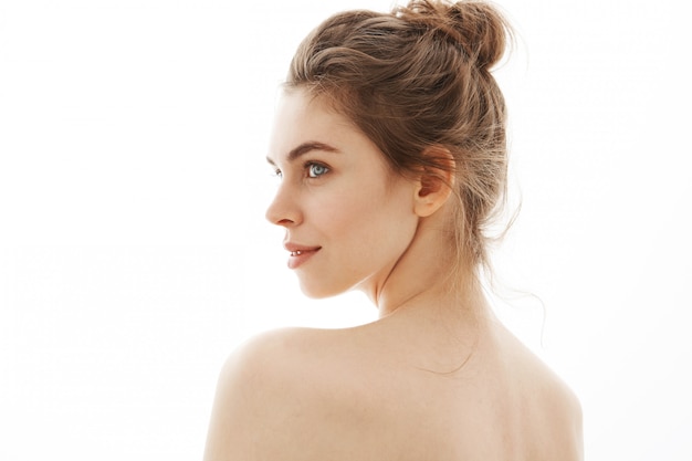 Portrait de jeune belle femme nue tendre avec chignon debout sur fond blanc.