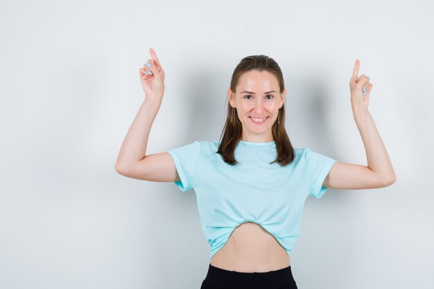 Portrait de jeune belle femme pointant vers le haut en t-shirt et regardant joyeuse vue de face