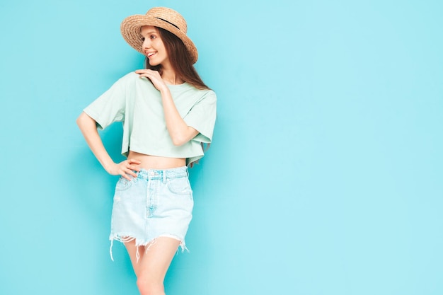 Portrait de jeune belle femme souriante en jeans d'été à la mode jupe femme insouciante posant près du mur bleu en studio Modèle positif s'amusant à l'intérieur Enthousiaste et heureux Au chapeau