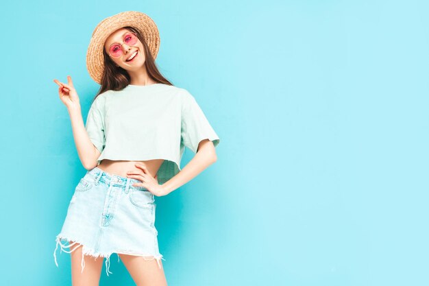 Portrait de jeune belle femme souriante en jeans d'été à la mode jupe femme insouciante posant près du mur bleu en studio Modèle positif s'amusant à l'intérieur Enthousiaste et heureux Au chapeau