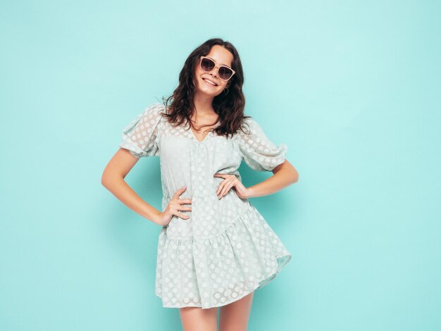 Portrait de jeune belle femme souriante en robe d'été à la modeFemme insouciante sexy posant près du mur bleu en studioModèle positif s'amusant à l'intérieurGai et heureux