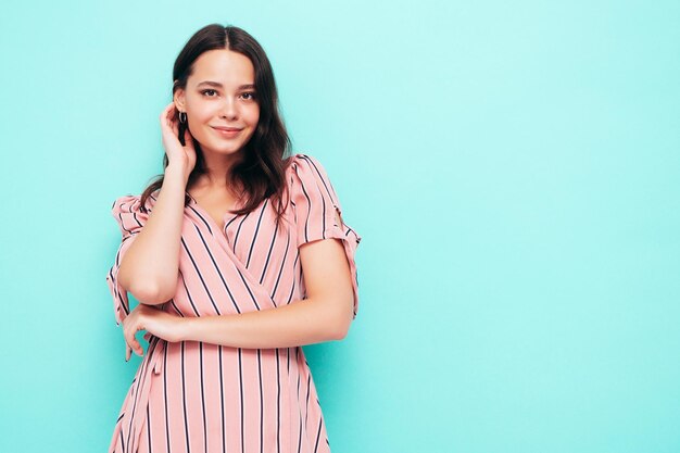 Portrait de jeune belle femme souriante en robe rose d'été à la mode Sexy femme insouciante posant près du mur bleu en studio Modèle positif s'amusant à l'intérieur Enthousiaste et heureux