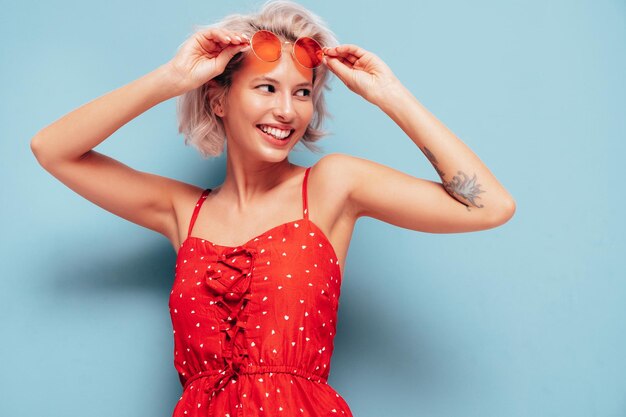 Portrait de jeune belle femme souriante en robe rouge d'été à la mode Sexy femme insouciante posant près du mur bleu en studio Modèle blond positif s'amusant et devenant fou Enthousiaste et heureux