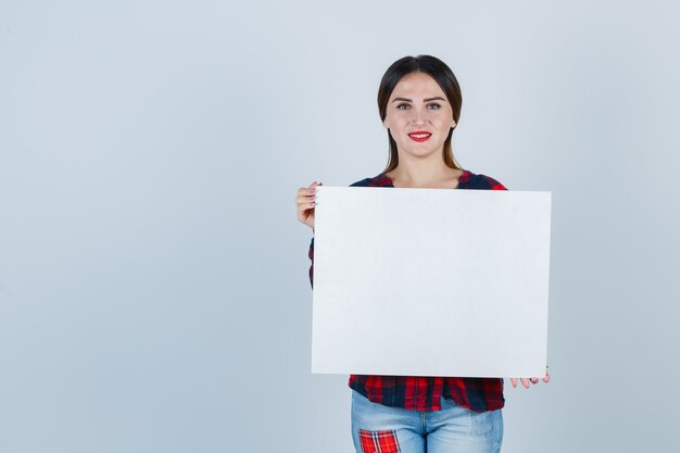 Portrait de jeune belle femme tenant un tableau blanc en chemise décontractée et à la vue de face heureuse