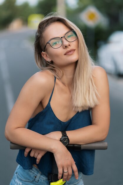 Portrait jeune belle fille dans les lunettes équitation un scooter électrique en été dans la rue