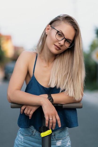 Portrait jeune belle fille dans les lunettes équitation un scooter électrique en été dans la rue