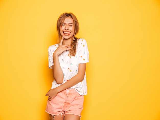 Portrait de jeune belle fille souriante hipster en jeans d'été à la mode shorts vêtements. Sexy femme insouciante posant près du mur jaune. Modèle positif s'amusant et montrant la langue
