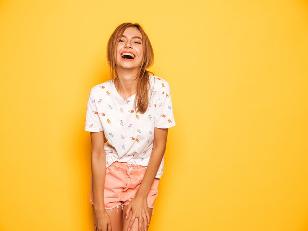 Portrait de jeune belle fille souriante hipster en jeans d'été à la mode shorts vêtements. Sexy femme insouciante posant près du mur jaune. Modèle positif s'amusant