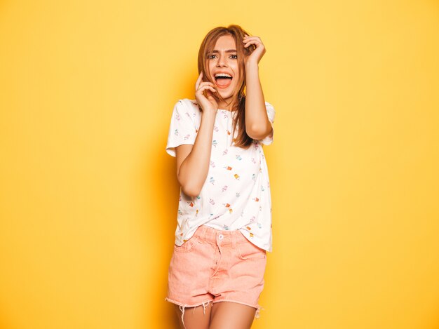 Portrait de jeune belle fille souriante hipster en jeans d'été à la mode shorts vêtements. Sexy femme insouciante posant près du mur jaune. Modèle positif s'amusant