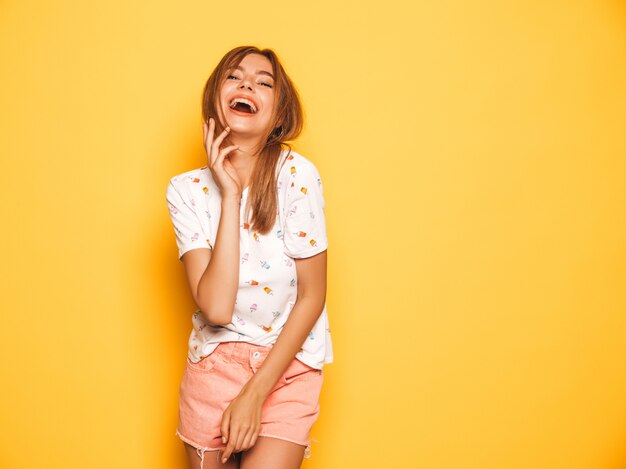 Portrait de jeune belle fille souriante hipster en jeans d'été à la mode shorts vêtements. Sexy femme insouciante posant près du mur jaune. Modèle positif s'amusant