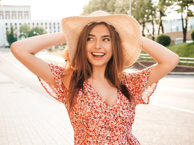 Portrait de jeune belle fille souriante hipster en robe d'été à la mode. Sexy femme insouciante posant sur le fond de la rue en chapeau au coucher du soleil. Modèle positif à l'extérieur