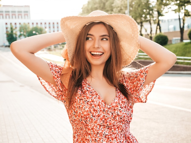 Portrait de jeune belle fille souriante hipster en robe d'été à la mode. Sexy femme insouciante posant sur le fond de la rue en chapeau au coucher du soleil. Modèle positif à l'extérieur