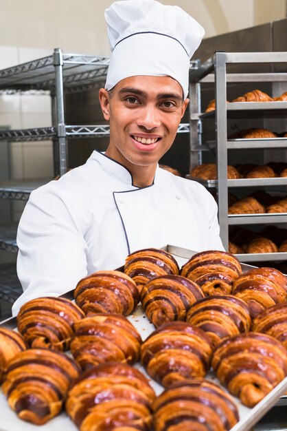 Portrait d&#39;un jeune boulanger homme souriant tenant un plateau de croissant frais