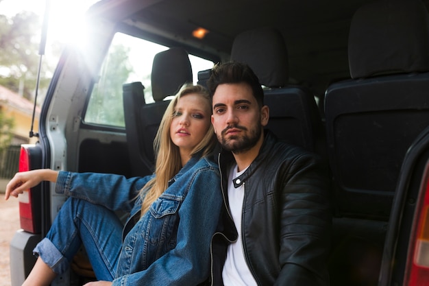 Portrait d&#39;un jeune couple assis sur le coffre de la voiture