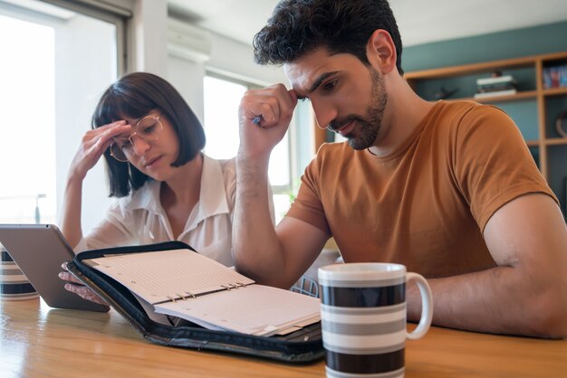 Portrait de jeune couple calcul et paiement des factures sur tablette numérique à domicile. Planification du budget mensuel du couple.