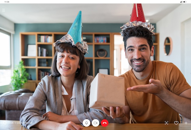 Portrait de jeune couple célébrant son anniversaire lors d'un appel vidéo avec une boîte-cadeau de la maison