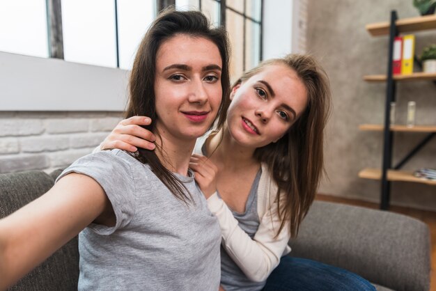 Portrait d&#39;un jeune couple de lesbiennes souriant assis sur un canapé prenant selfie