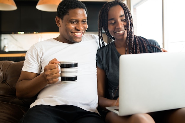 Portrait de jeune couple, passer du temps ensemble et utiliser un ordinateur portable assis sur un canapé à la maison. Nouveau concept de mode de vie normal.