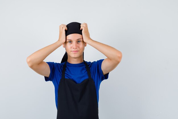 Portrait de jeune cuisinier homme avec les mains sur la tête en t-shirt, tablier et à la vue de face oublieux