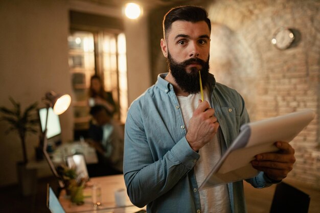 Portrait d'un jeune entrepreneur analysant des rapports d'activité tout en travaillant la nuit au bureau