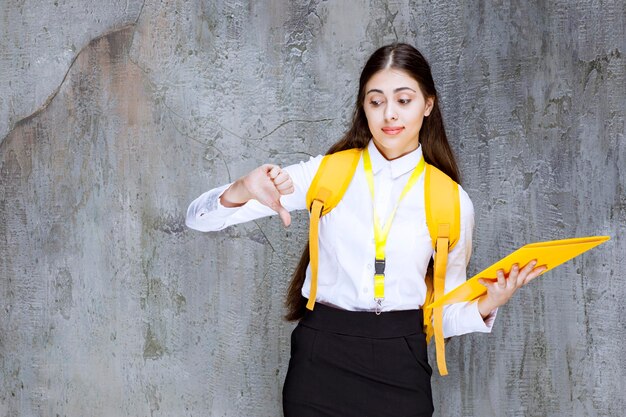 Portrait de jeune étudiante avec cahier jaune donnant les pouces vers le bas. Photo de haute qualité