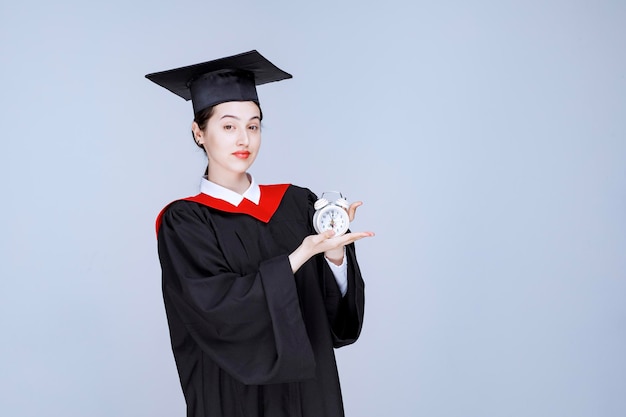 Portrait de jeune étudiante diplômée tenant une horloge pour afficher l'heure. photo de haute qualité