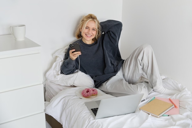 Photo gratuite portrait d'une jeune étudiante qui étudie dans son lit et se détend en préparant ses devoirs.