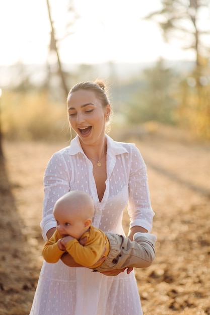 Portrait de jeune famille attrayante avec petit bébé, posant dans la belle forêt de pins d'automne à la journée ensoleillée. Bel homme et sa jolie femme brune