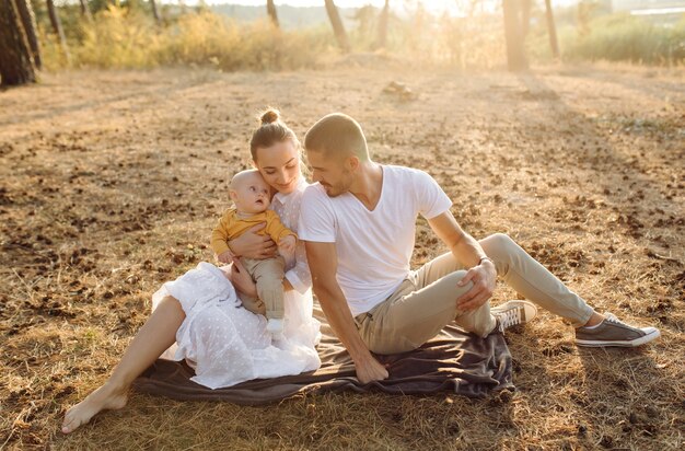 Portrait de jeune famille attrayante avec petit bébé, posant dans la belle forêt de pins d'automne à la journée ensoleillée. Bel homme et sa jolie femme brune