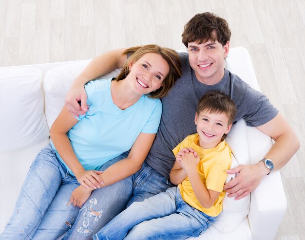 Portrait de jeune famille heureuse en riant avec fils en casuals sur le canapé à la maison - high angle