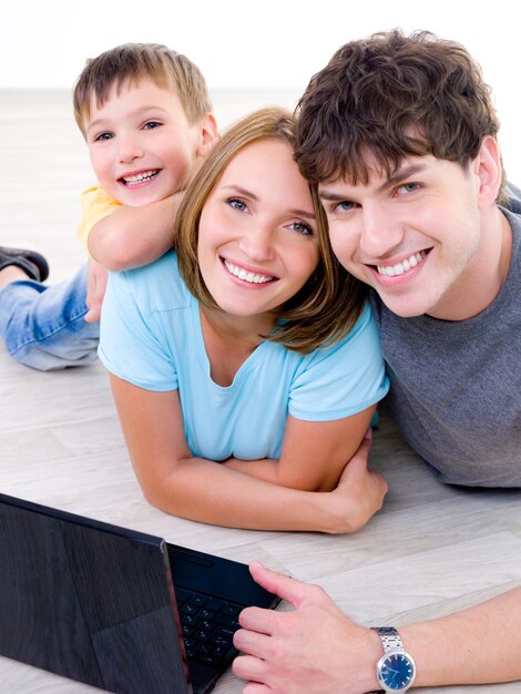 Portrait de jeune famille heureuse en riant avec petit fils et avec ordinateur portable - à l'intérieur