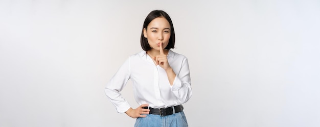 Portrait de jeune femme adulte asiatique chut dire chut chut presse le doigt sur les lèvres partage secret ne parle pas geste tabou debout sur fond blanc