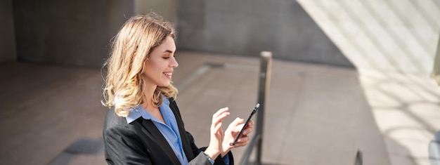 Photo gratuite portrait d'une jeune femme d'affaires sur un escalator utilisant un smartphone et souriante en appuyant sur un téléphone portable