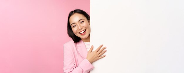 Portrait de jeune femme d'affaires japonaise femme d'entreprise en costume pointant sur le mur avec un graphique montrant un diagramme ou une publicité sur fond rose espace copie vide