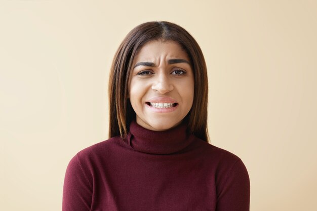 Portrait de jeune femme afro-américaine brune dégoûtée frustrée fronçant les sourcils et grimaçant à cause d'une odeur dégoûtante ou puante, serrant les dents. Mauvaise odeur, dégoût et émotions négatives