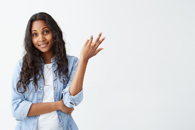 Portrait de jeune femme afro-américaine douteuse à la recherche de perplexité isolé sur mur blanc. Agréable femme à la peau sombre vêtue d'une chemise en jean ayant confus et incertain