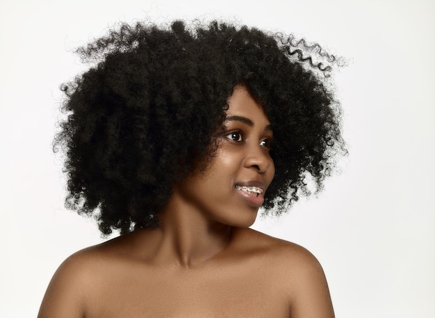 Portrait de jeune femme afro-américaine noire souriante et surprise avec des bretelles sur un mur blanc