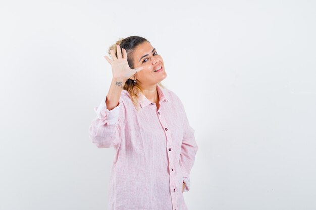 Portrait de jeune femme en agitant la main pour dire au revoir en chemise rose et à la vue de face heureuse