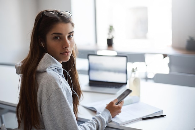 Portrait de jeune femme à l'aide d'un ordinateur portable et d'un téléphone intelligent à la recherche d'une nouvelle maison à louer sur son prêt étudiant